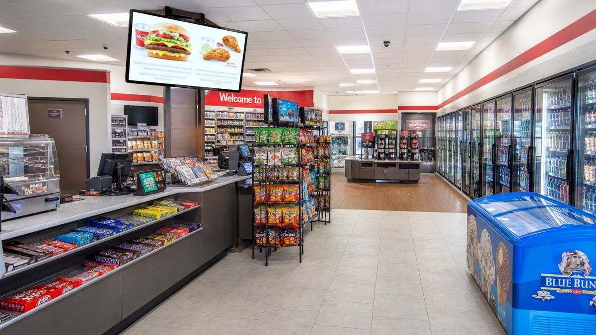 A brightly lit convenience store interior showing the checkout counter and an active digital video signage display promoting a local store special. A brightly lit convenience store interior showing the checkout counter and an active digital video signage display promoting a local store special.
