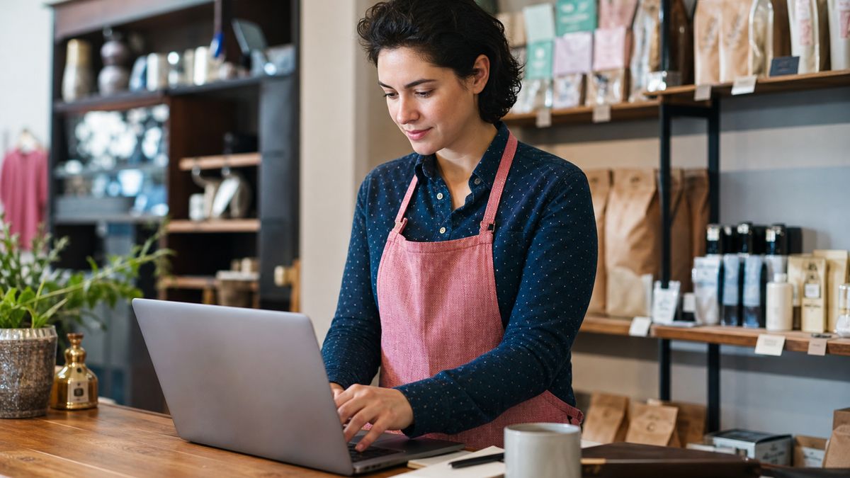 A business owner smiling and using a laptop inside a local shop to configure a digital video campaign on an easy-to-use software dashboard.